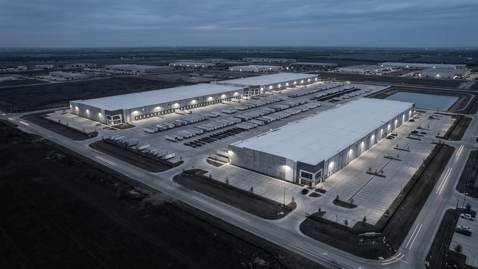 Aerial view of a light industrial campus at dusk with tilt-wall buildings, truck courts, and staged trailers