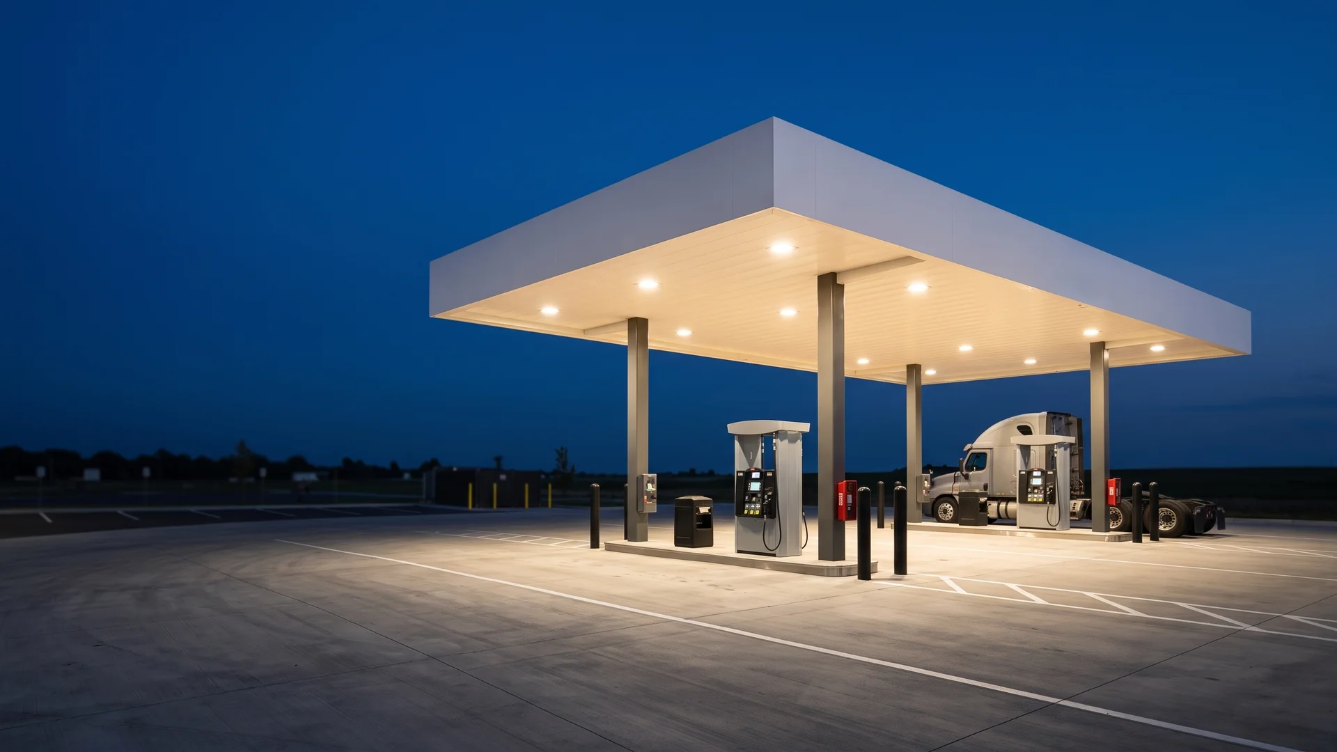 Fleet fueling canopy lit at dusk over concrete islands with a semi tractor at the far lane