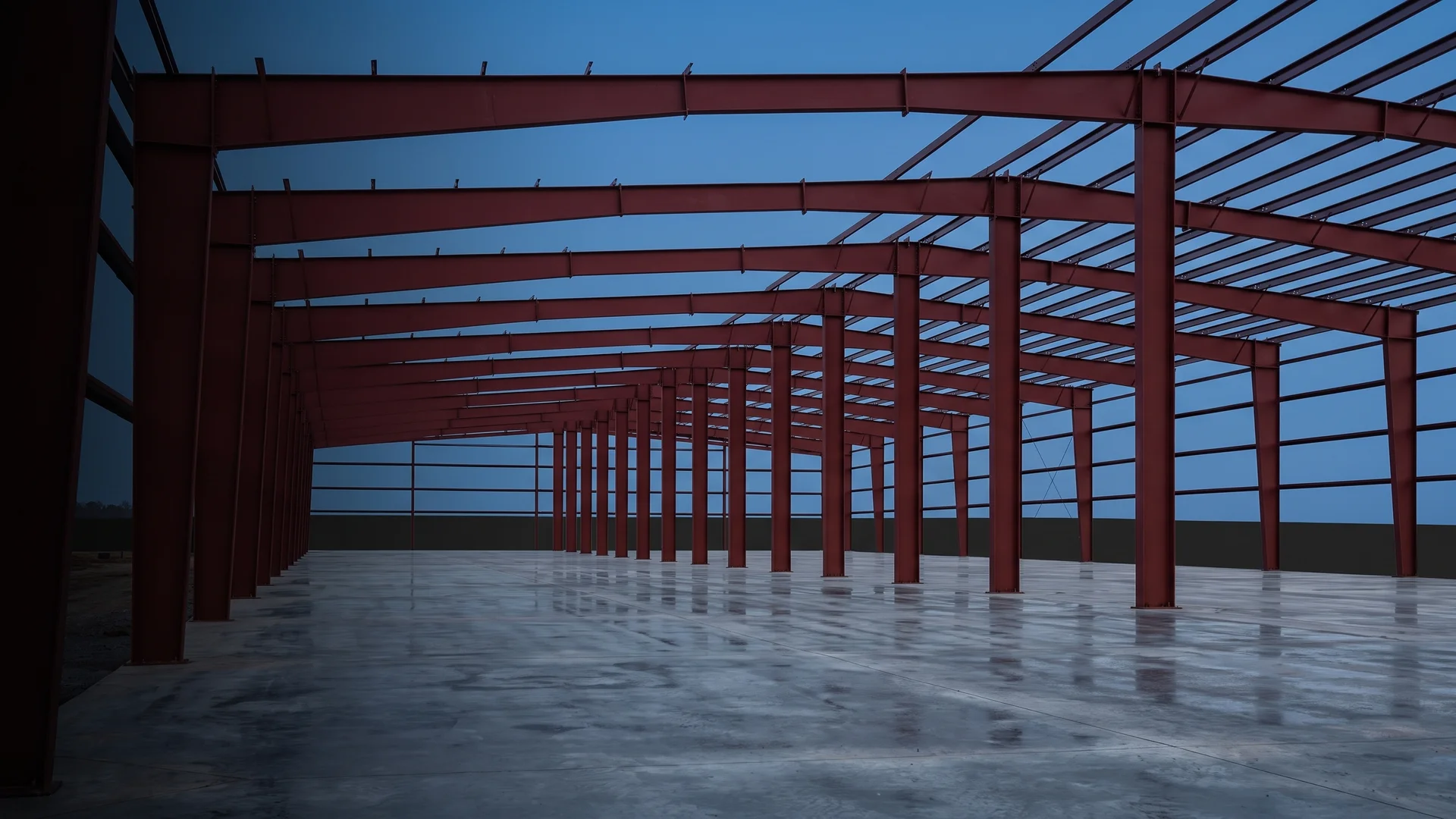 Row of freshly erected red steel frames for a pre-engineered metal building against a dusk sky
