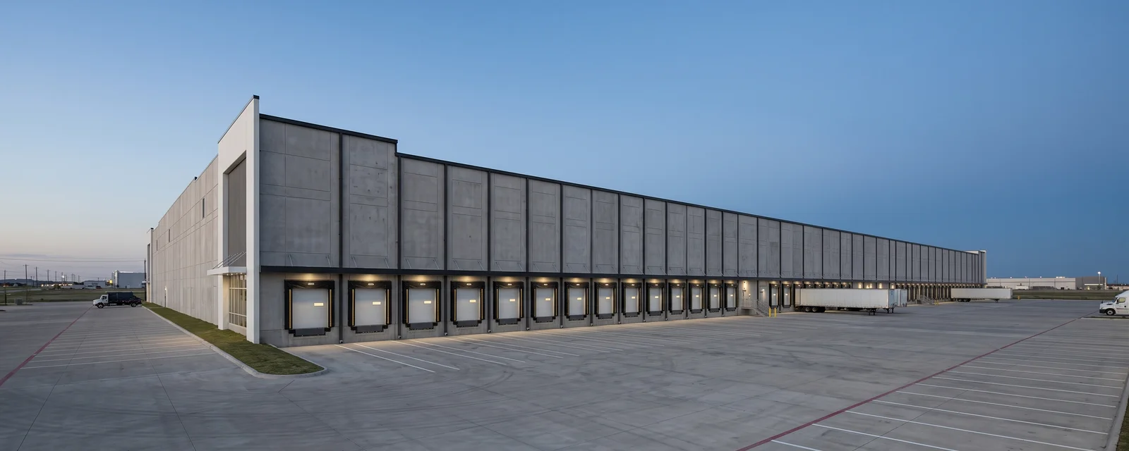 Completed tilt-wall distribution facility at dusk with a row of dock doors and a wide truck court