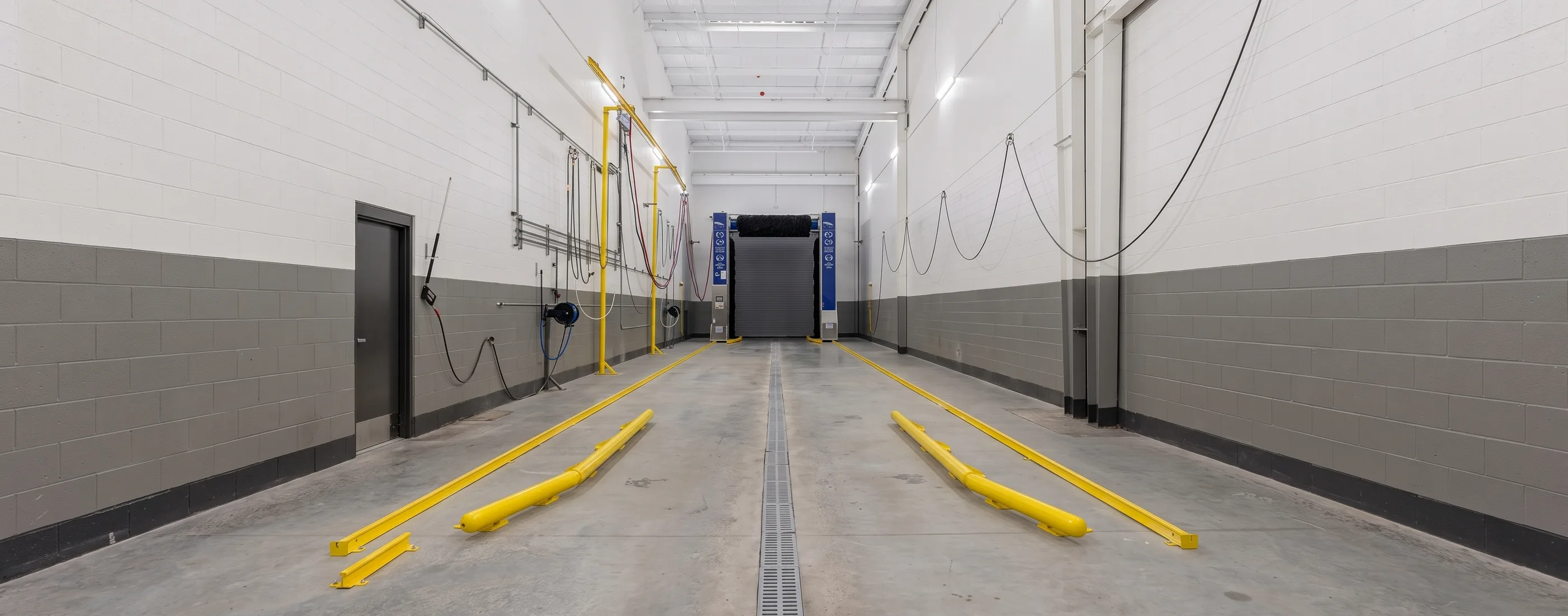 Truck wash bay with overhead hose reels and drainage trench