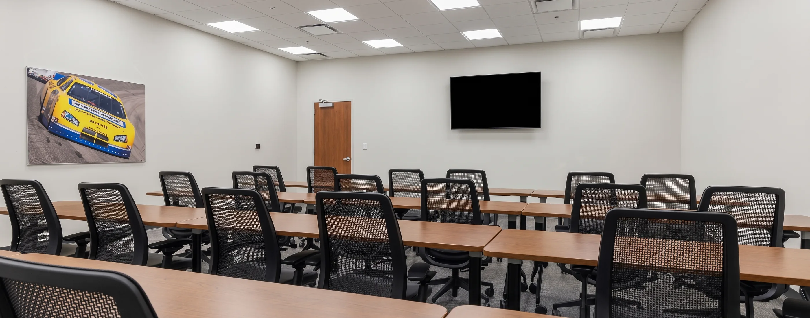 Training room with rows of tables, chairs, and a wall-mounted display